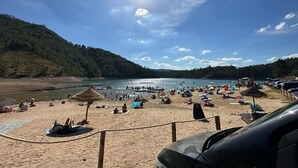Ein Strand mit Holzfence, Sonnenschirmen und entspannten Menschen.