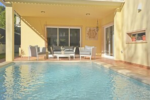 A covered outdoor area with a pool, seating, and potted plants.