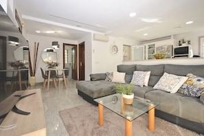 A modern living room with a grey sofa, a glass coffee table, and a dining area with a wooden table and chairs.