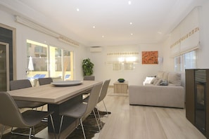 A modern living room with a dining area, a sofa, a TV, and a plant.
