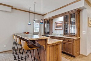 Una cocina con barra, armarios de madera y luces colgantes.