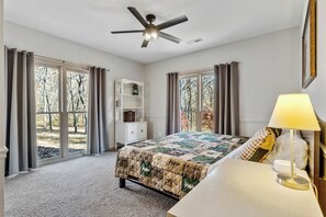 Un dormitorio con cama, mesita de noche con lámpara, ventilador de techo y ventana con cortinas.