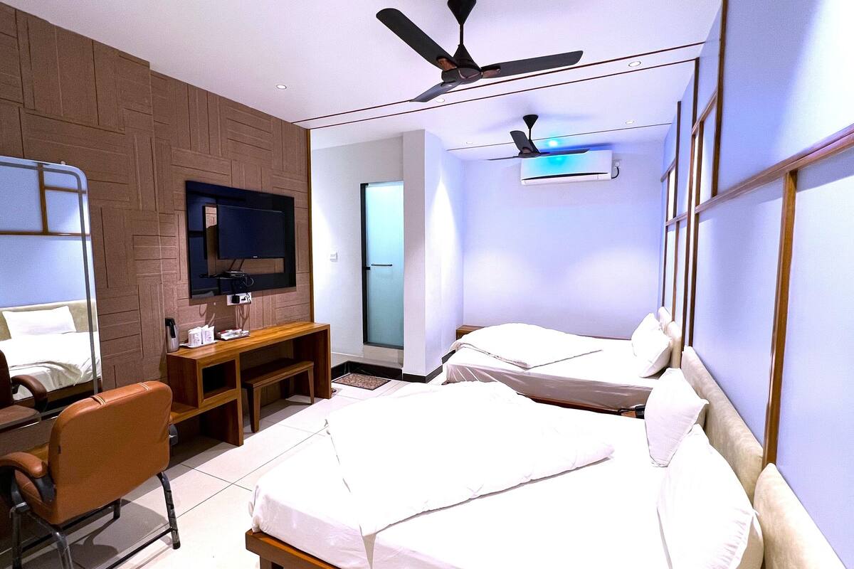 A hotel room with two beds, a TV, a desk, a chair, and a ceiling fan.