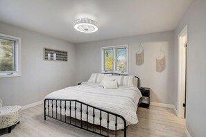 A bedroom with a bed, bedside tables, a chair, a window with blinds, and a chandelier. - Draper Vacation Home - Families & Friends Welcome (Baraboo)