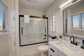 A modern bathroom with a glass shower enclosure, a white toilet, a sink with a black faucet, and a mirror with a decorative frame. - Draper Vacation Home - Families & Friends Welcome (Baraboo)