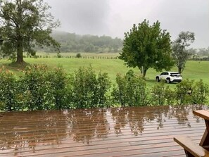 Una terraza de madera con vistas a un campo cubierto de hierba y un vehículo blanco.