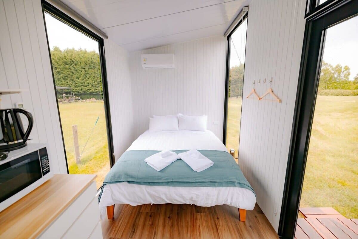 Quarto de hotel pequeno e estreito, com uma cama, micro-ondas e vista para uma área gramada através de amplas janelas.