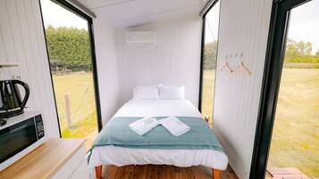 Quarto de hotel pequeno e estreito, com uma cama, micro-ondas e vista para uma área gramada através de amplas janelas.
