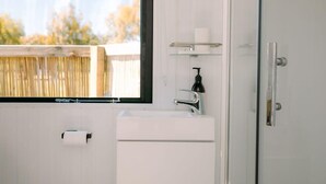 Ein Badezimmer mit einem weißen Waschbecken, einem Spiegel, einem Toilettenpapierhalter und einem Regal mit einer Flasche.