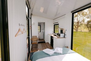 Une chambre à coucher de taille réduite, comprenant un lit, un bureau et donnant sur un espace verdoyant.