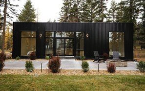 A modern black building with large windows, a concrete porch, and outdoor seating.