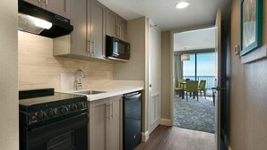 A compact kitchen with a stove, microwave, and dishwasher. It leads to a balcony with a view. - Nature's Front-Row: 11th Floor Palms King Suite (Myrtle Beach)