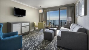 A hotel room with a sofa, armchair, TV, and a balcony with a view. - Nature's Front-Row: 14th Floor Palms King Suite (Myrtle Beach)