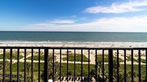 Blick auf einen Strand vom Balkon mit Geländer, feinem Sand und Meer.