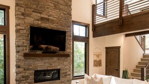 Amplia sala de estar con chimenea de piedra, un sofá blanco y una escalera que lleva a un nivel superior.
