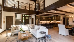 Un salón espacioso con un sofá blanco grande, una mesa de centro de madera y una alfombra estampada. Se ve, al fondo, un comedor con una mesa y sillas de madera.
