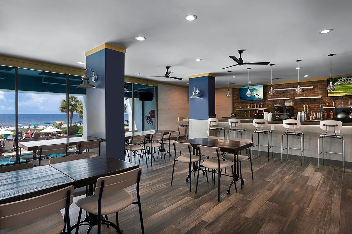 A modern restaurant with wooden flooring, bar area, and large windows offering a view of the ocean.