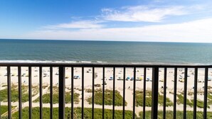 A beach with a clear view of the ocean and a balcony railing in the foreground.