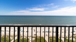 A beach with umbrellas and people, viewed from a balcony with a railing. - Sunrise and Sunset Views: 14th Floor Palms Suite (Myrtle Beach)