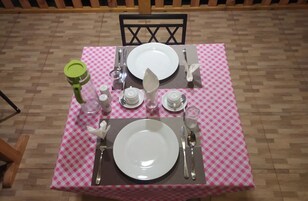 Una mesa de comedor dispuesta con platos, cubiertos, vasos y una botella de agua.