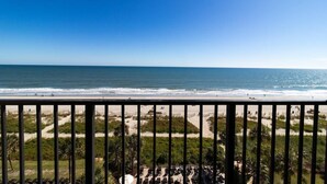 Blick auf einen Strand vom Balkon mit Geländer, feinem Sand und dem Meer.