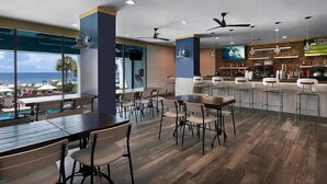 Um restaurante moderno com piso de madeira, área de bar e grandes janelas com vista para o mar.