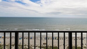 Vista da praia a partir de uma varanda com grade, praia de areia e oceano.