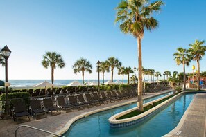 A poolside area with lounge chairs, palm trees, and a view of the ocean. - Escape to Coastal Comfort: 10th Floor Palms Suite (Myrtle Beach)