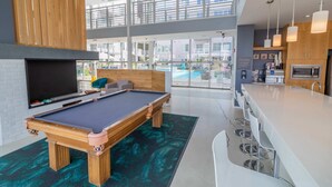 Une table de billard dans une pièce moderne, dotée d’une grande fenêtre, d’un coin bar et d’une cuisine.