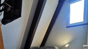 A small, sloped room with a single bed, a nightstand, a lamp, and a window. - Modernes Nurdachhaus in Fedderwardersiel für bis zu 5 Personen und Hund (Butjadingen)