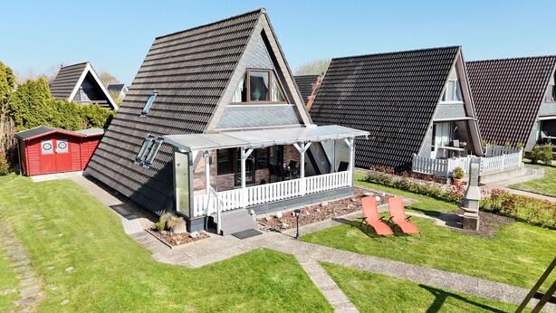 A modern house with a sloped roof, a covered porch, and a red shed. - Modernes Nurdachhaus in Fedderwardersiel für bis zu 5 Personen und Hund (Butjadingen)