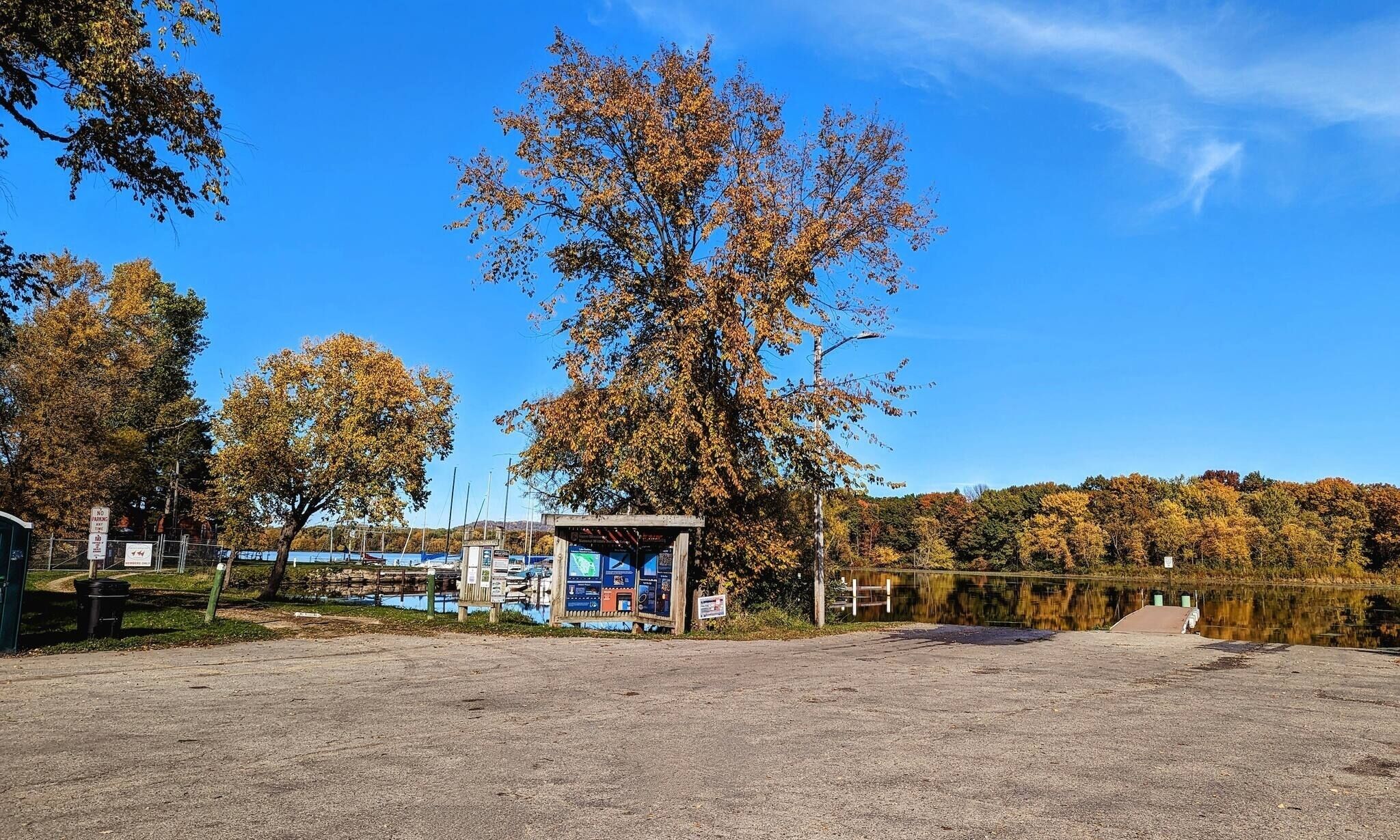 A lakeside park with a small pavilion, a dirt path, and a fence.