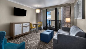 Habitación de hotel con sofá, reposapiés, televisor y un pequeño comedor con sillas y mesa.