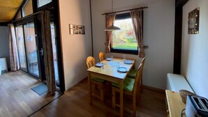 Un comedor con una mesa de madera dispuesta para cuatro personas, una ventana con cortinas y vistas a zonas verdes.