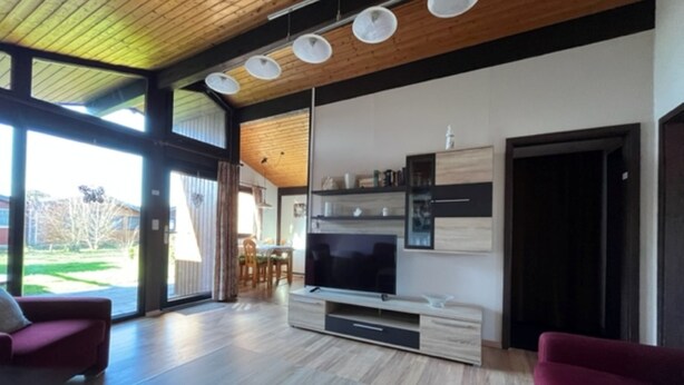 Un salón moderno con un televisor grande, suelo de madera y sofás rojos.