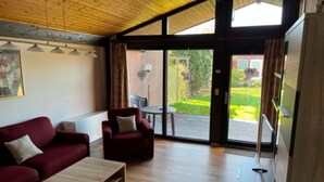 Una sala de estar moderna con techo de madera, un sofá rojo, una mesa de centro de madera y un puerta corrediza de vidrio que da a un espacio exterior.