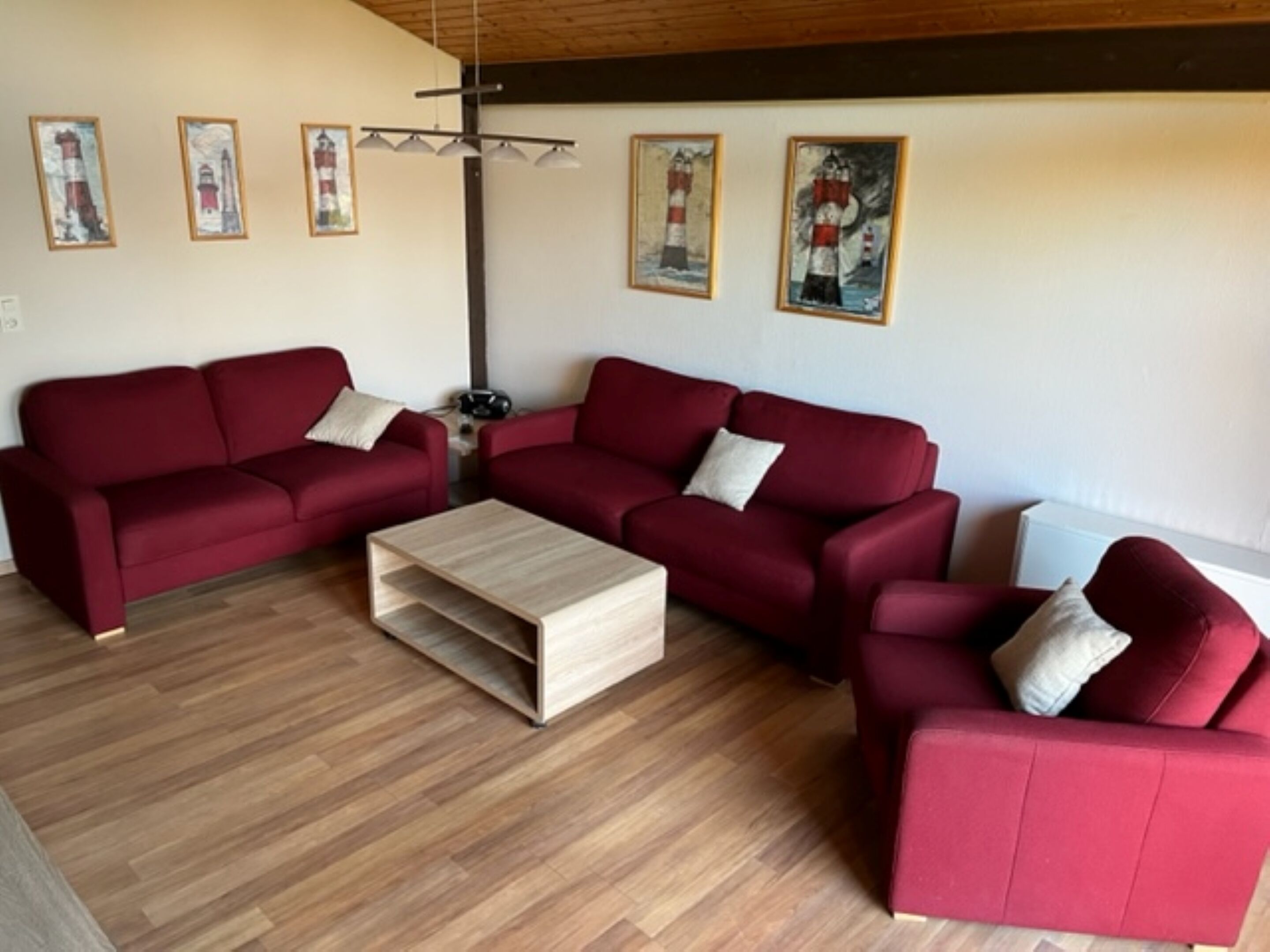 A living room with two red sofas, a wooden coffee table, and four framed artworks on the wall.