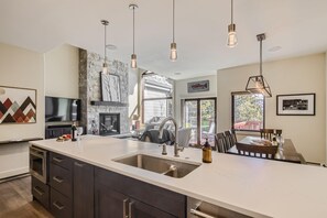 A modern kitchen with a large island, stainless steel appliances, pendant lighting, and a view to the outdoors. - Tall Pines Chalet | True Ski In/Ski Out | Renovated (Breckenridge)