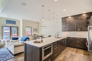 Une cuisine moderne avec des meubles en bois foncé, des appareils électroménagers en acier inoxydable et des luminaires suspendus.