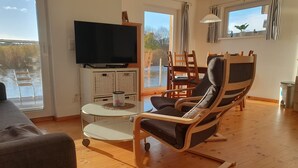 Ein Wohnzimmer mit Fernseher, Korbmöbeln, einem Glastisch und Blick auf einen See.