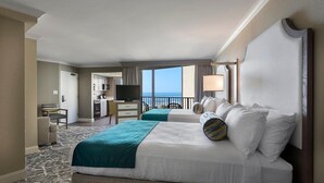Quarto de hotel com duas camas, uma escrivaninha, televisão e vista para o oceano.