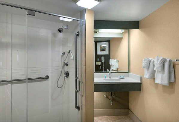 Une salle de bain d’hôtel avec une douche en verre, un lavabo avec un miroir et des serviettes accrochées au mur.