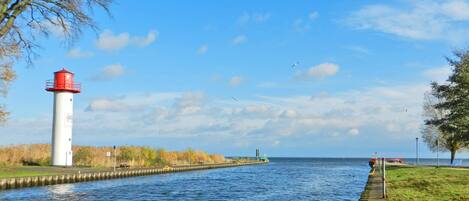 A calm waterway with a lighthouse on the left, a grassy bank on the right, and a clear sky.