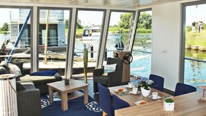 Ein modernes Interieur mit großen Fenstern, einem Essbereich und Blick auf Boote auf dem Wasser.