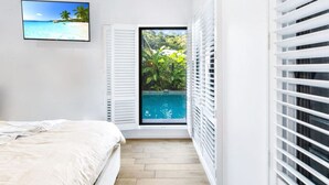 Ein Schlafzimmer mit einem Bett, einem Fernseher an der Wand und einem Fenster mit Jalousien.