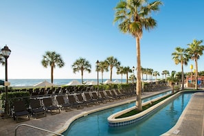 Ein Poolbereich mit Liegestühlen, Palmen und Blick auf das Meer.
