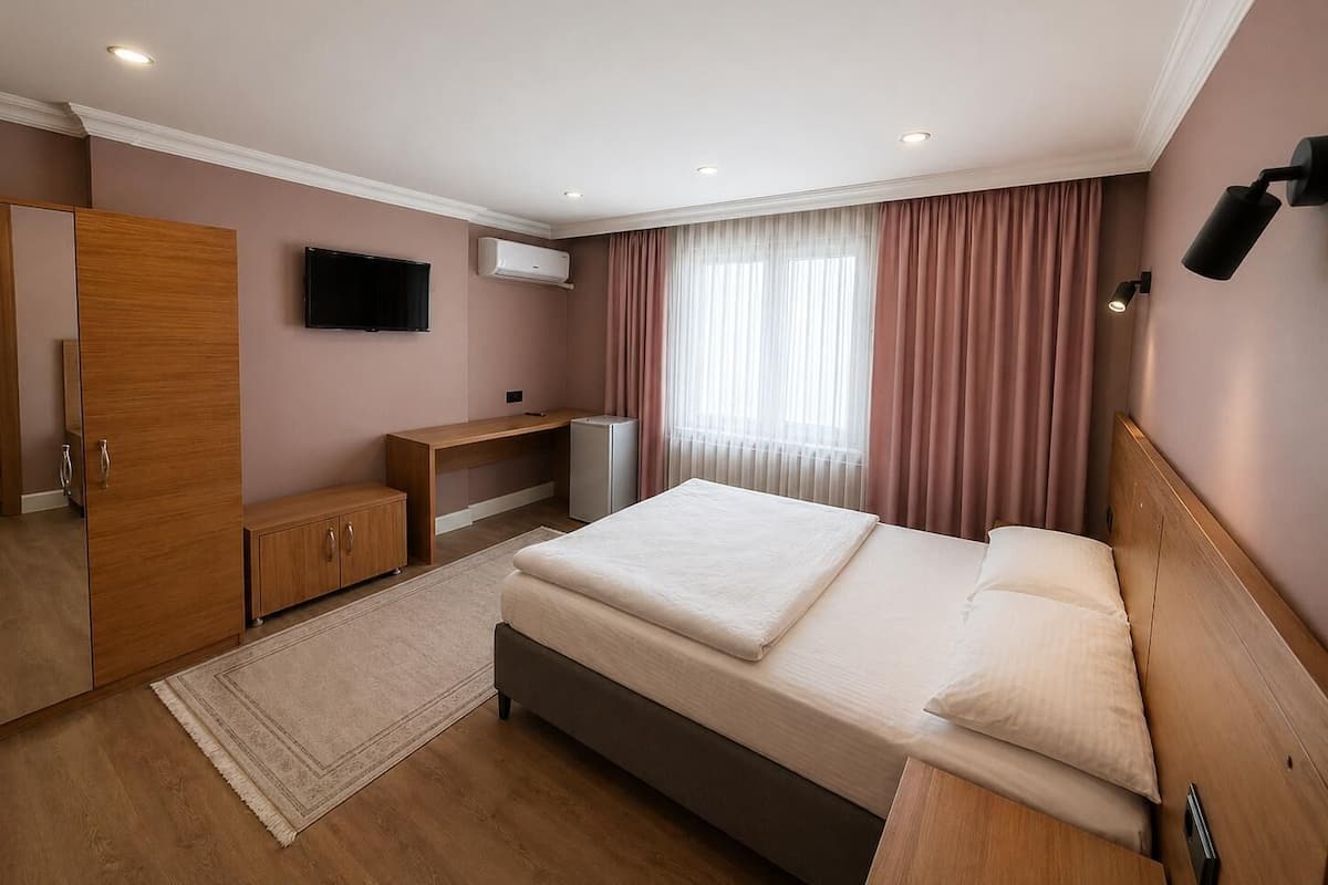 A hotel room with a bed, a desk, a wardrobe, a television, and an air conditioning unit.