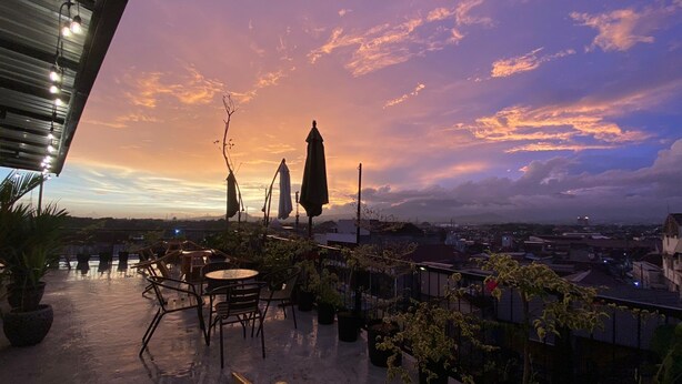 Une terrasse sur le toit, aménagée avec des espaces de détente en plein air, des plantes en pot et offrant une vue sur le panorama urbain au coucher du soleil.