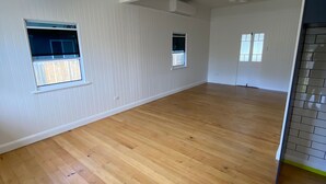 A spacious room with wooden flooring, white walls, and two small windows.
