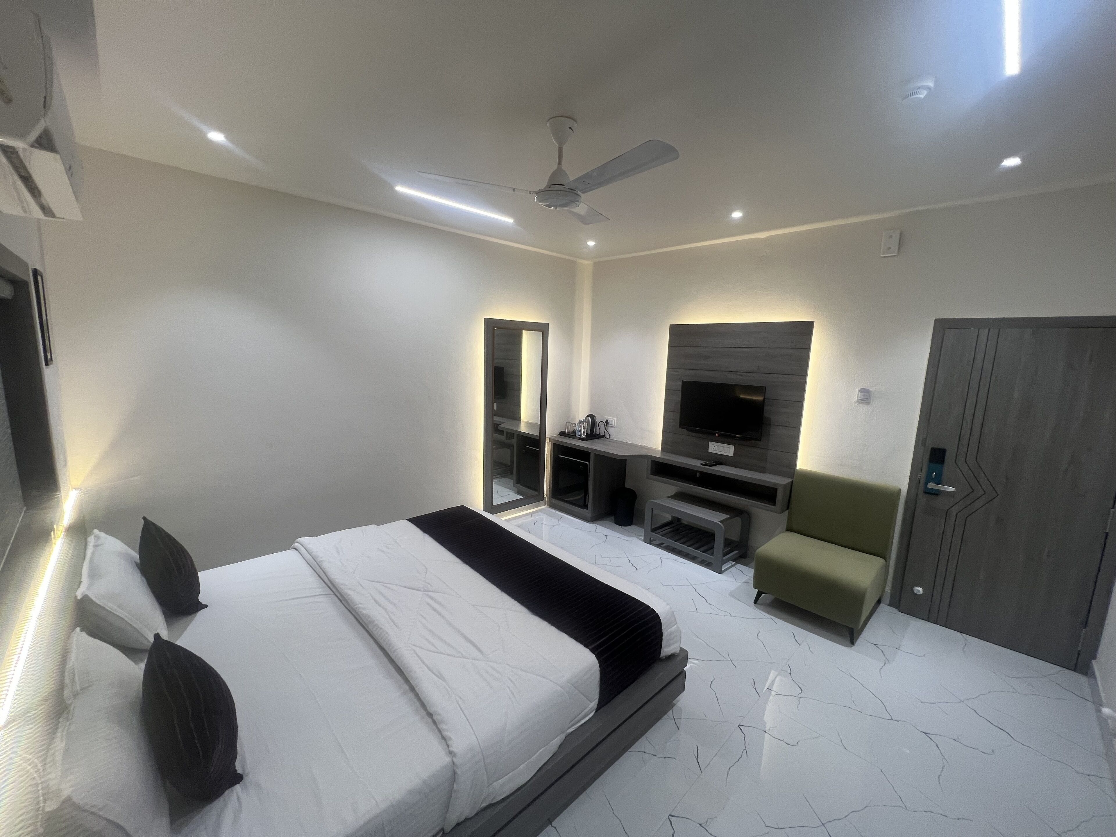 A modern hotel room with a large bed, a flat-screen TV mounted on the wall, a seating area with a small table and chairs, and a door with a unique design.